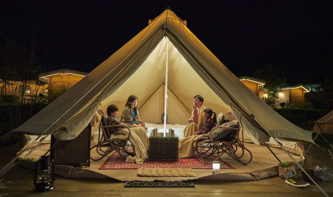 four people sitting in an open, lit tipi at night