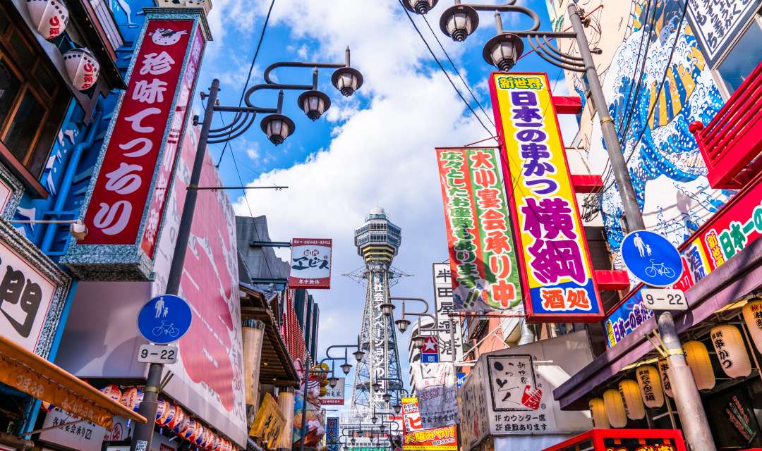 a brightly colored street with shop signs and a tower