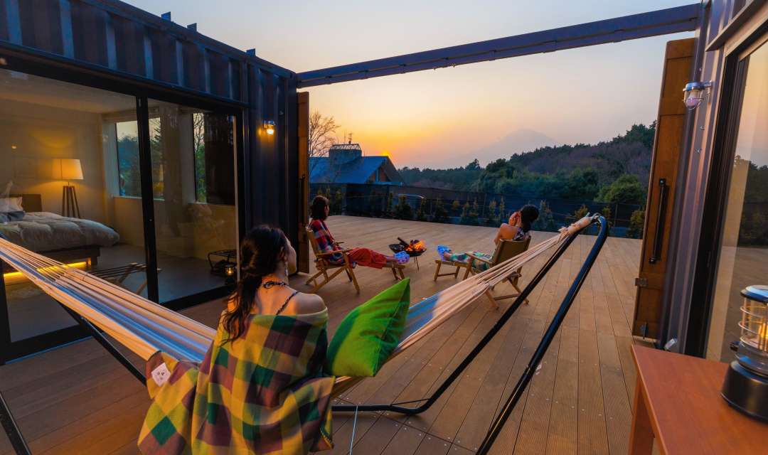 three women in hammocks and on chairs on a wooden terrace at sunset