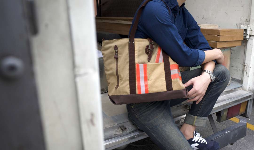 A man sitting down wearing a blue shirt and a beige bag