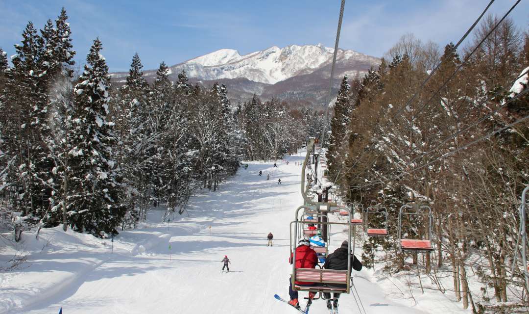 people on a ski lift going over a ski slope surrounded by trees