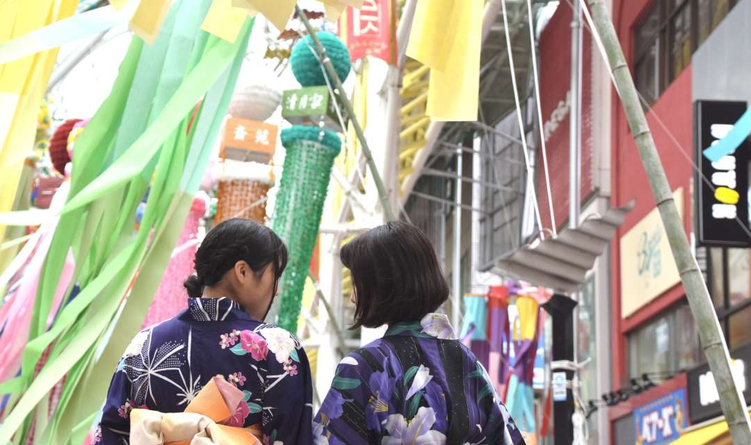 the back of two women in yakata standing in front of festive streamers on a street