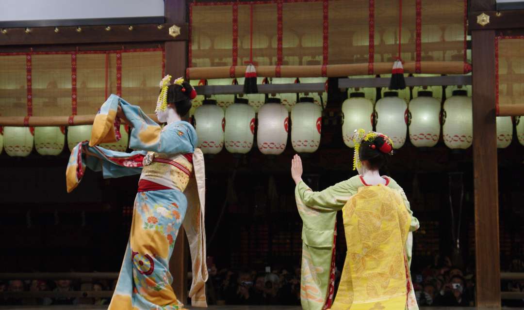 Two geisha dancing on a stage decorated with lanterns