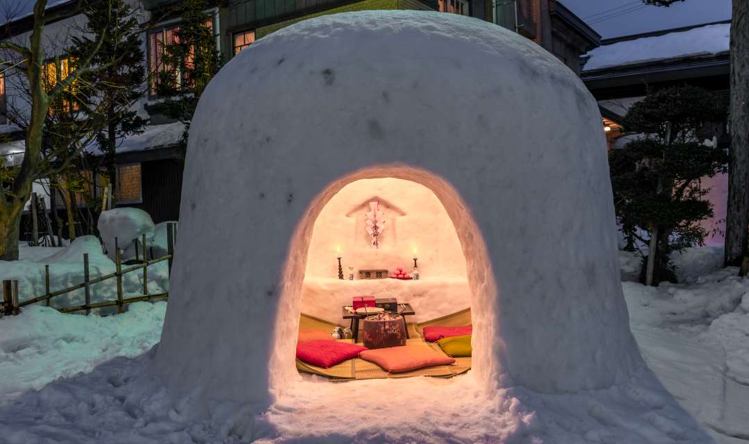 cushions and candles inside a kamakura igloo on the snowy ground on a dark night