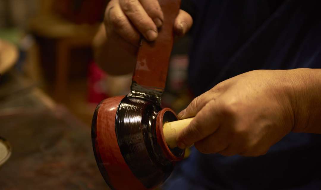 a pair of hands painting a dark ceramic bowl