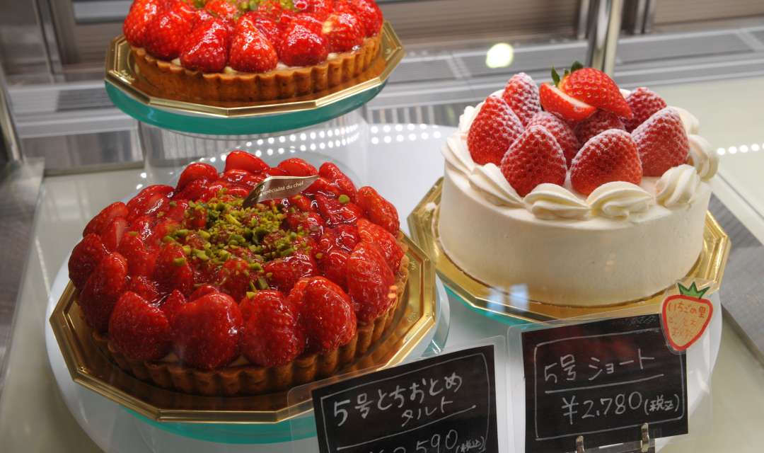 three strawberry and cream cakes and tarts in a fridge