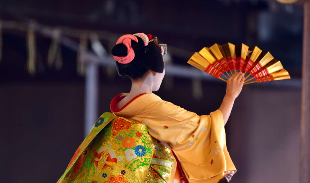 Back of a woman wearing a yellow kimono and holding a fan