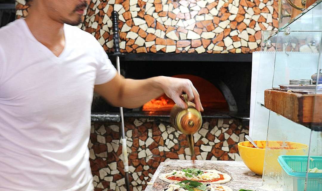 A man pouring oil onto uncooked pizzas