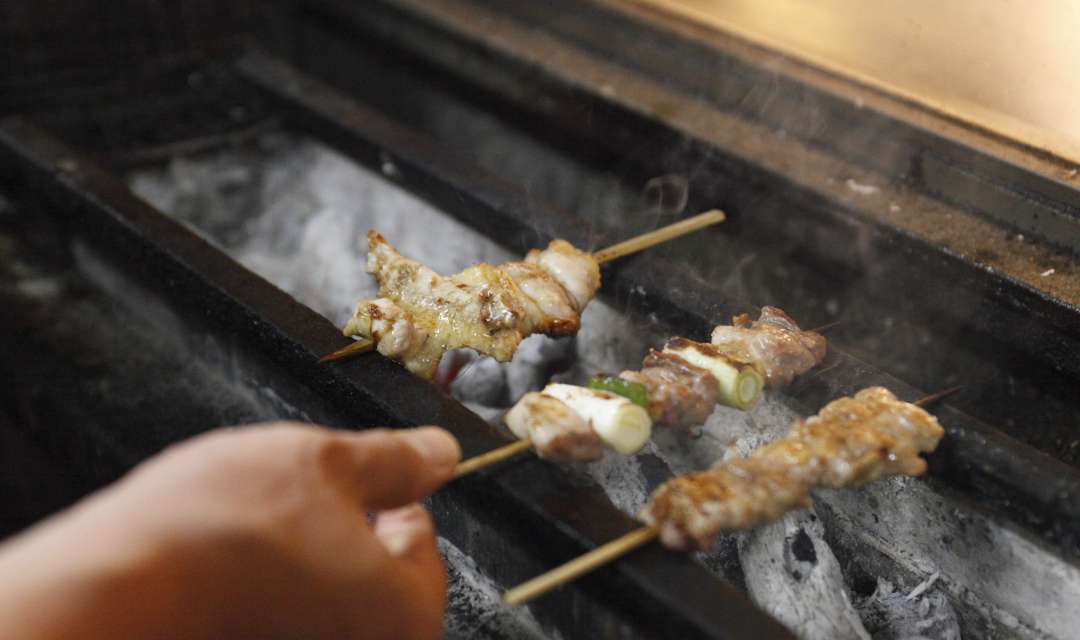 yakitori chicken and leeks being grilled on coals