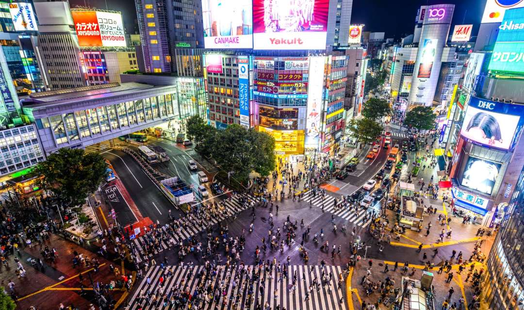 aerial view of busy street at night with people crossing roads and neon lights