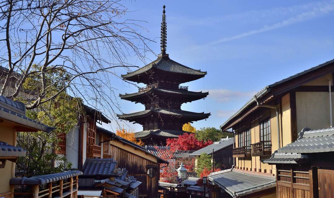 A storied pagoda surrounded by autumn trees and traditional Japanese houses