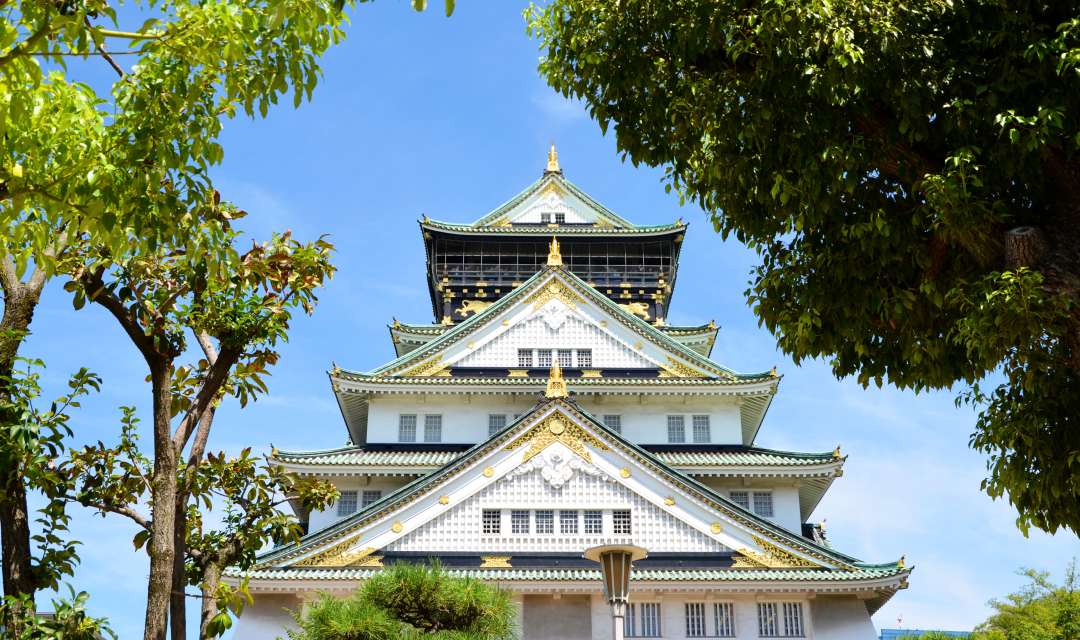 Japanese Castle against a blue sky, with trees either side of it