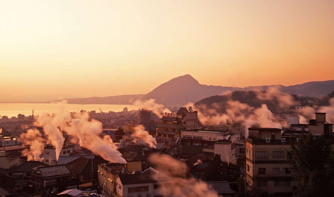 A townscape with mountain backdrop and steaming onsens