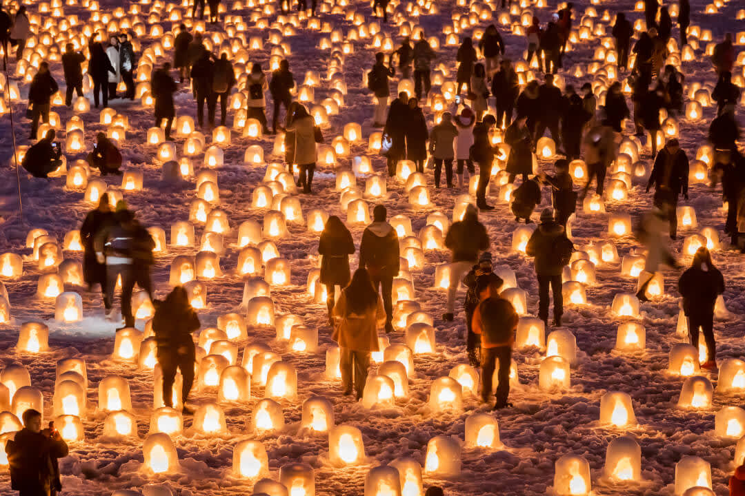 People walking amongst miniature lit up snow huts at the Yokote Kamakura Festival in Akita Prefecture