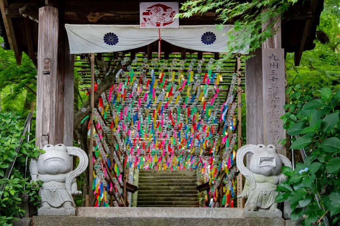 Two frog statues flanking an entrance covered with colourful wind chimes in Nyoirinji Temple, Fukuoka Prefecture