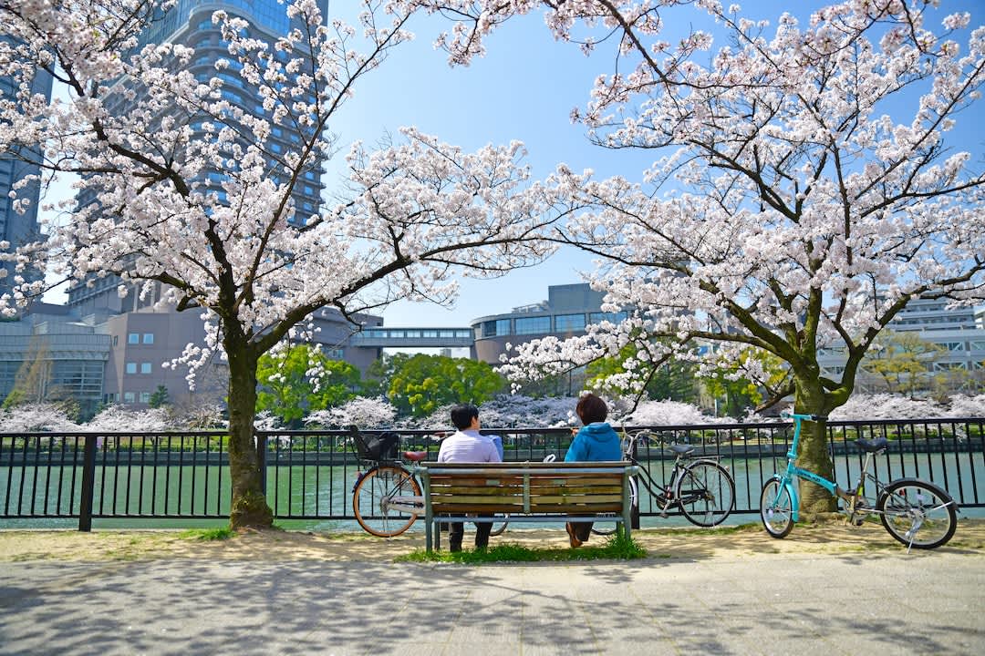 Two people resting on a bench at Kema Sakuranomiya Park alongside the Ogawa River, Osaka.