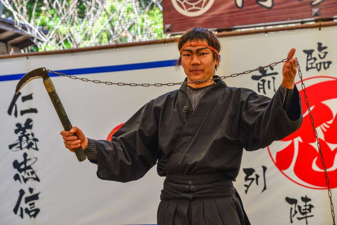 Man in a Ninja outfit showcasing a weapon at Ninja Museum of Igaryu, Mie Prefecture.