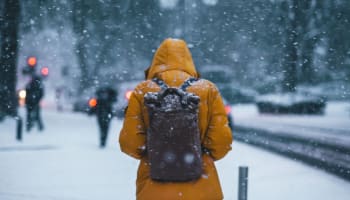 a person wearing a yellow jacket and backpack walking in the snow
