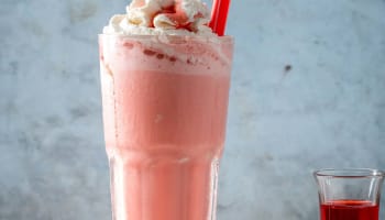 a glass of pink liquid on a wooden surface