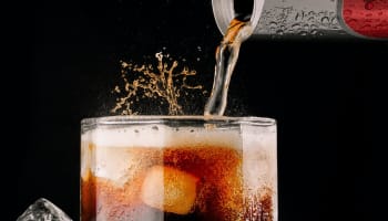 a glass of liquid with ice and a black background