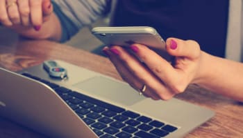 a hand holding a phone and using a laptop