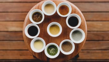a group of small white cups with different sauces on a wooden table