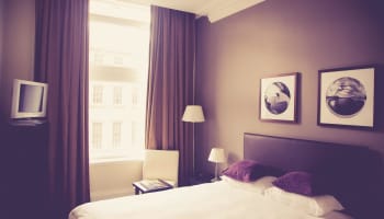 a bed with purple pillows and a chair in a room with a window