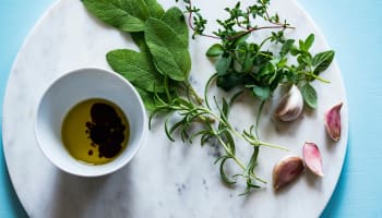 a bowl of oil and herbs on a marble surface