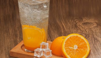 a wooden tray with a glass of orange juice and ice cubes