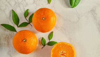 a group of oranges with leaves on a marble surface