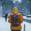 a person wearing a yellow jacket and backpack walking in the snow