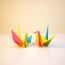 two colorful paper cranes on a white surface