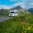 a white RV on a road with flowers and mountains in the background