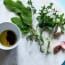 a bowl of oil and herbs on a marble surface