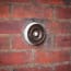 a round metal doorbell with a white light bulb on a brick wall