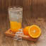 a wooden tray with a glass of orange juice and ice cubes