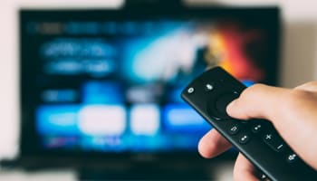 a hand holding a remote control in front of a television