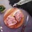 meat on a wooden board next to a bowl of peppers and a knife