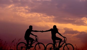 a silhouette of two people riding bicycles