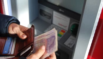 a person holding a wallet in front of an ATM