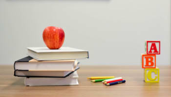 an apple on top of books and colored pencils