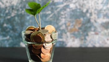 a plant growing from a glass cup of coins