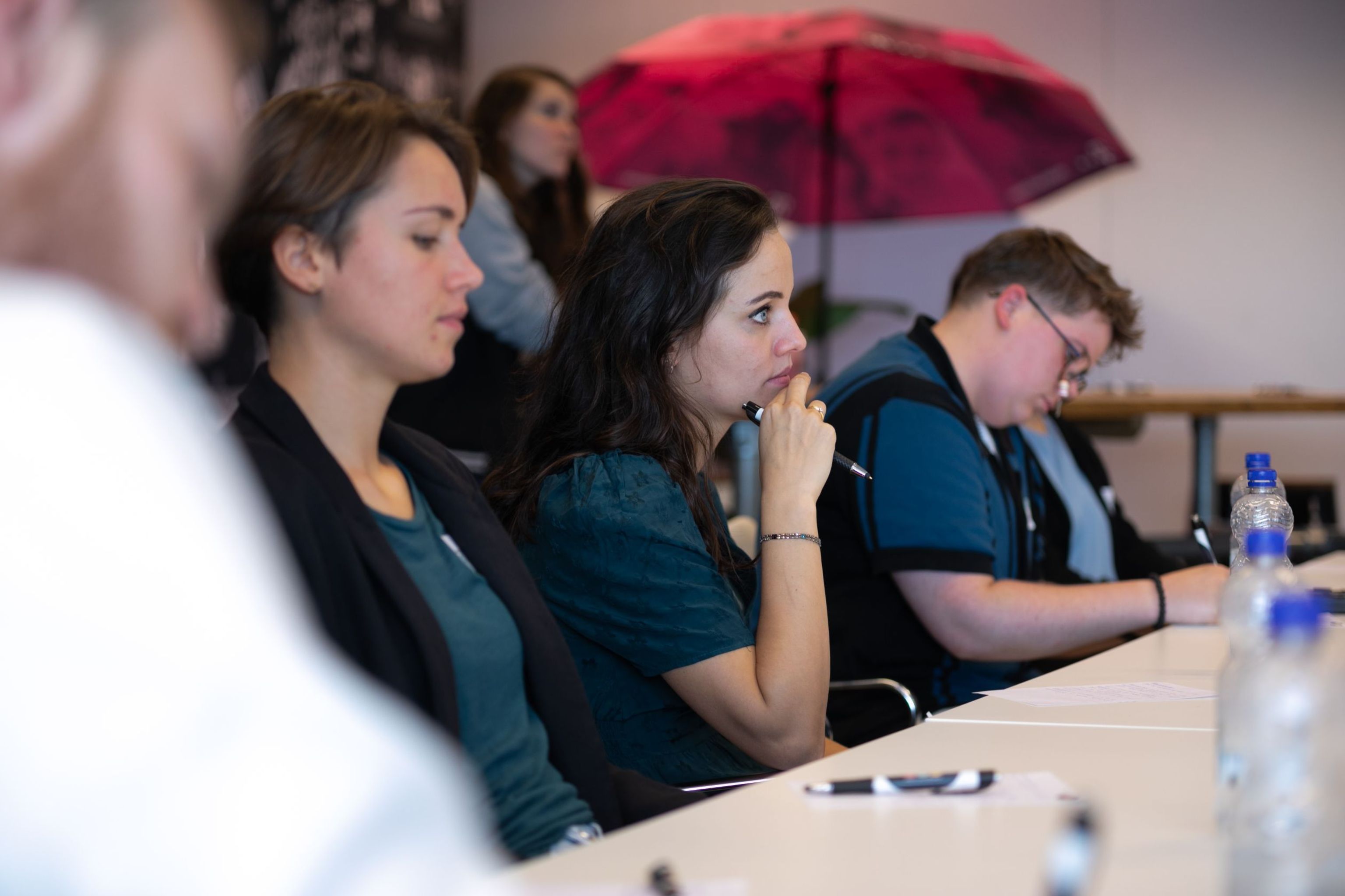 Drie personen die aan tafel zitten en naar een lezing luisteren