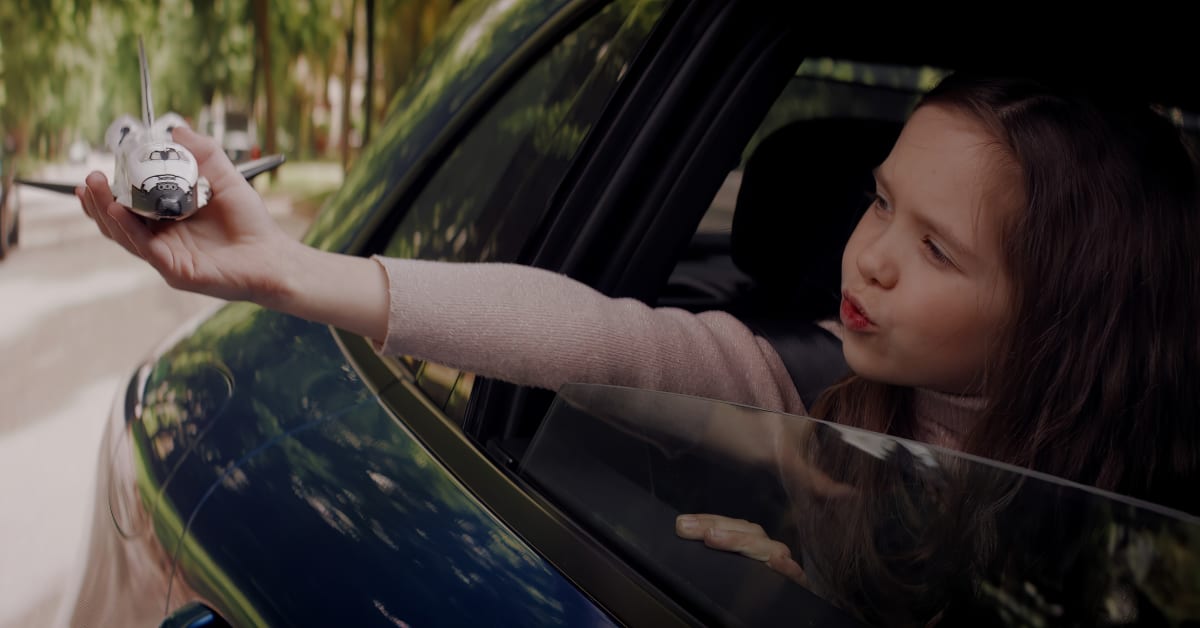 Cute little girl sticking her head out of a car window with a toy in her hand