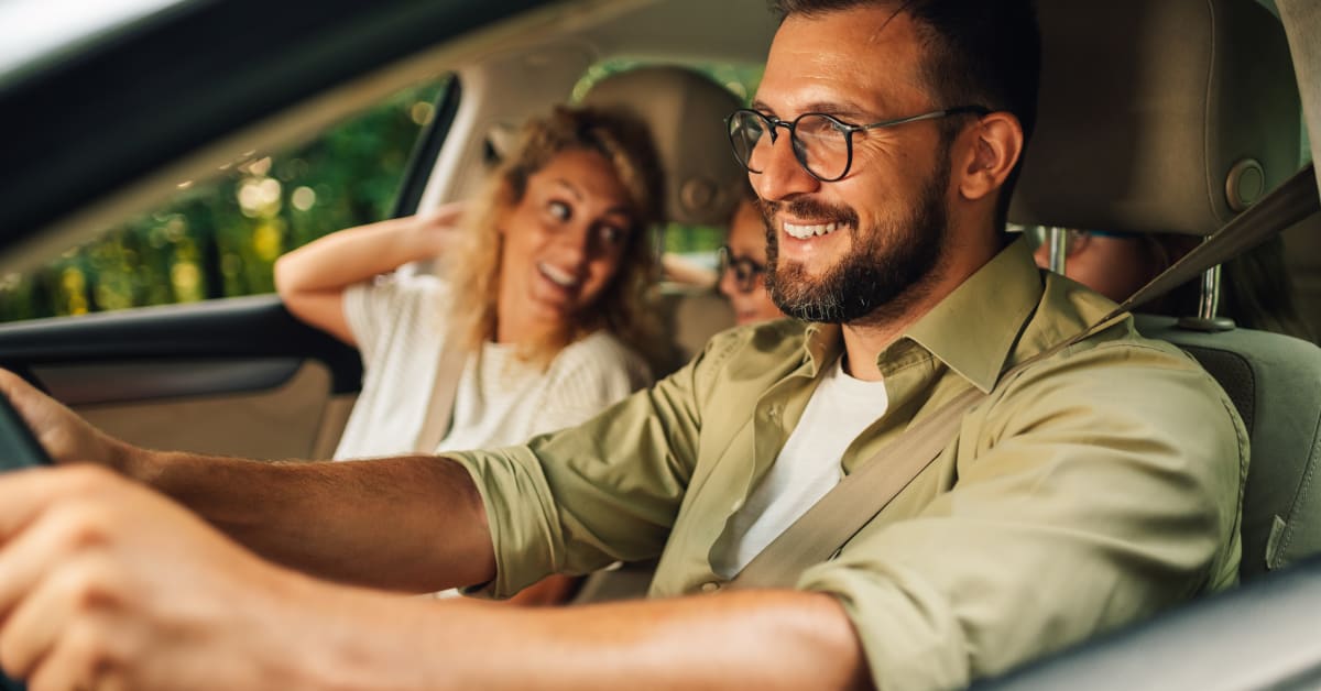 Dad driving a car while mom smiles at the kids in the backseat