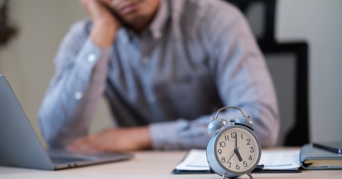 male at desk with chin in hand staring at clock
