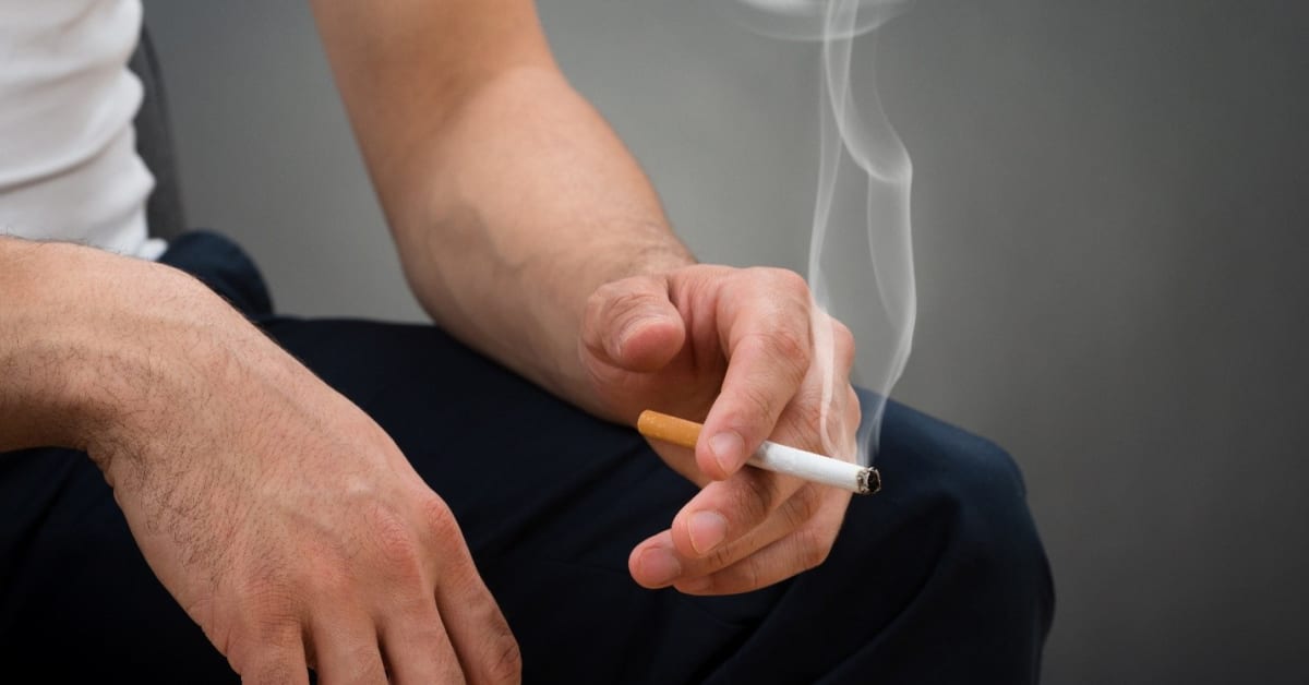Image of someone sitting while holding a cigarette