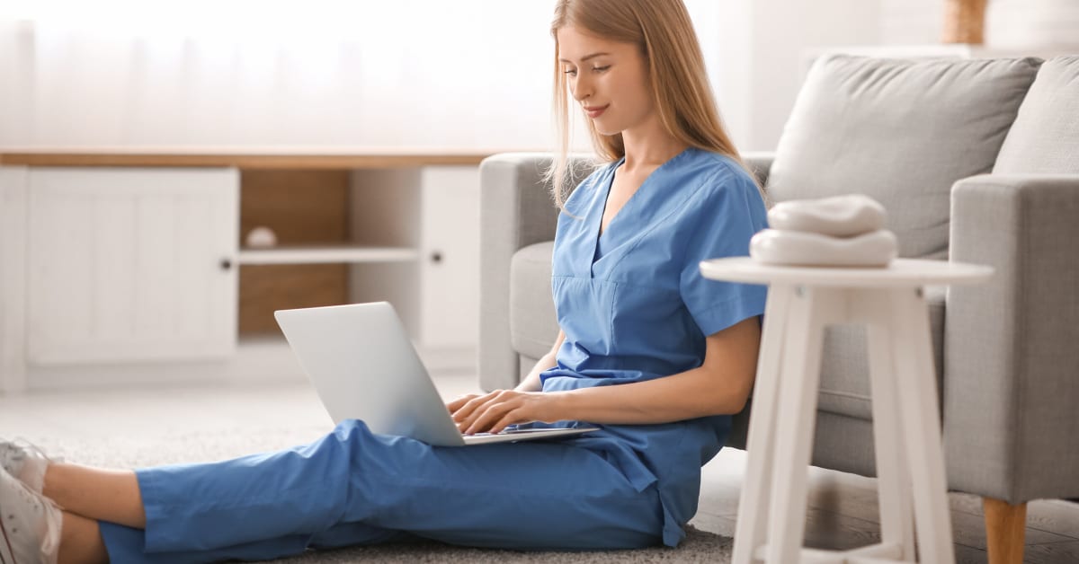 image of a nurse in scrubs on the floor on her laptop