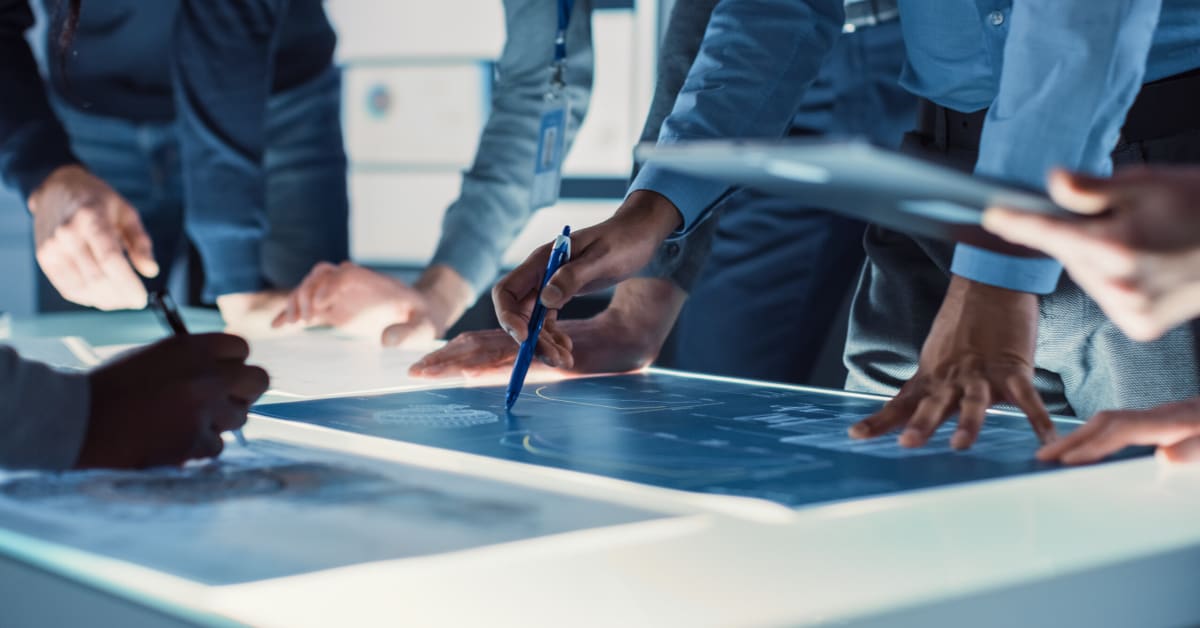 image of business people gathered around lightbox with plans on it