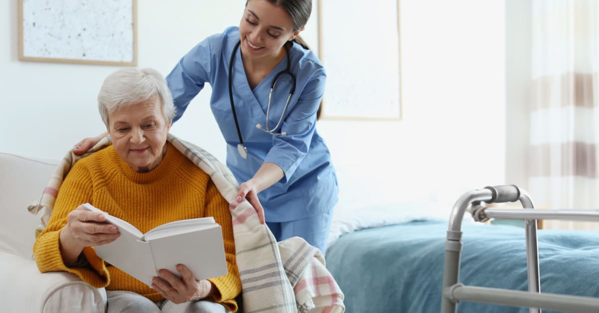 nurse putting a blanket on an elderly woman who is reading